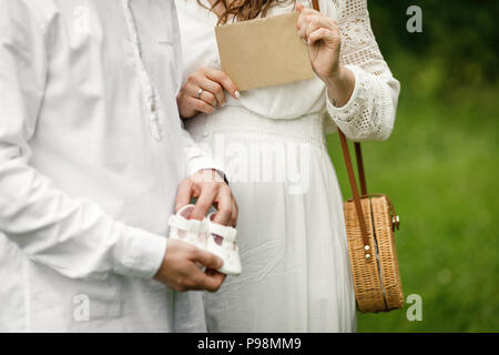 Glücklich und junge Schwangere Paar umarmen in der Natur. Schwangeren Paare ihre Zukunft baby boots Holding. Stockfoto