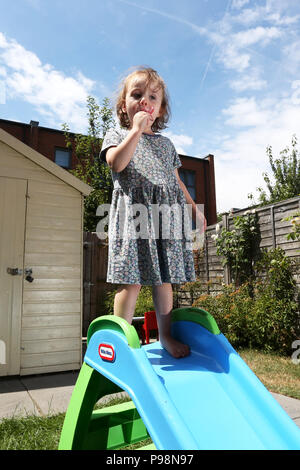 Ein junges Mädchen in einem Garten genießen Sie ein Eis in der Sonne in London, UK. Stockfoto