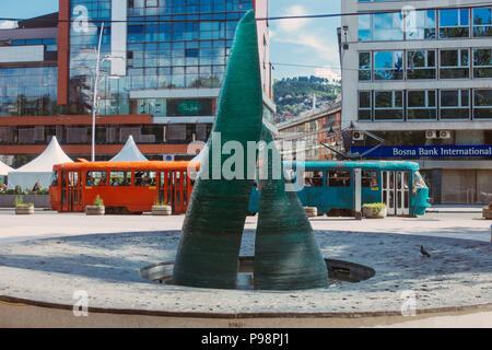 Eine Glasskulptur, die als Teil eines Gedenkens für die während der Belagerung von Sarajevo getöteten Kinder errichtet wurde. Hinter dem Hotel fährt eine Straßenbahn vorbei Stockfoto