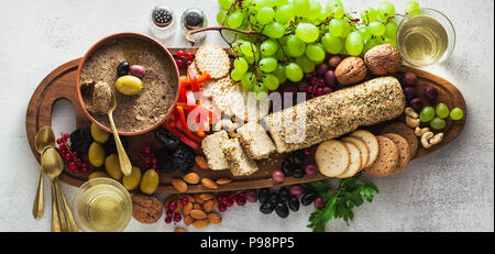 Banner der Holz-, das Board mit veganen Snacks. Pastete von Oliven und Käse aus cashewnüsse mit Kräutern. Gesunde Vorspeise mit Trauben, Nüssen, und Drie Stockfoto