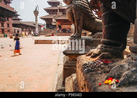 Kathmandu Tal, Kathmandu, Nepal: Passanten Spaziergang entlang der Unesco Patan Durbar Square. Auf vorne, zwei steinerne Löwen bewachen den Eingang zu Stockfoto