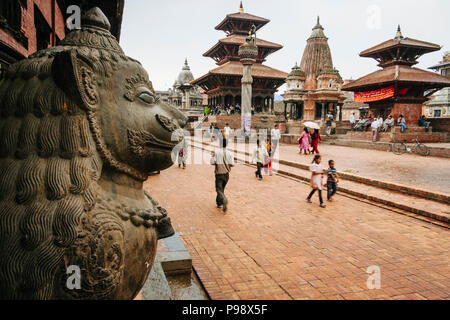Kathmandu Tal, Kathmandu, Nepal: Passanten Spaziergang entlang der Unesco Patan Durbar Square. Lion Statue ist ein Königlicher Palast ist im Vordergrund gesehen und Stockfoto