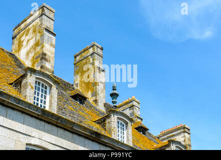 Das schieferdach mit Flechten bedeckt, die Dachfenster und Schornsteine eines Wohnhauses in der Altstadt von Saint-Malo, Frankreich, gegen den blauen Himmel. Stockfoto