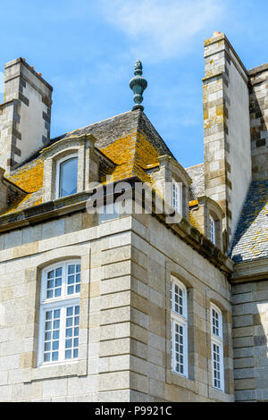 Die Oberseite eines Wohnhauses in der Altstadt von Saint-Malo mit einem Schieferdach bedeckt mit Flechten, Dachfenster und Schornsteine gegen den blauen Himmel. Stockfoto