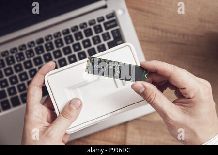 Man entpackt die neu erworbene M.2 SSD-Laufwerk über seinen Schreibtisch mit einem modernen Laptop Stockfoto