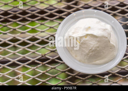 Schlagsahne in die weiße Schale auf dem Metall Tisch gegen Sonnenlicht Hintergrund. Stockfoto