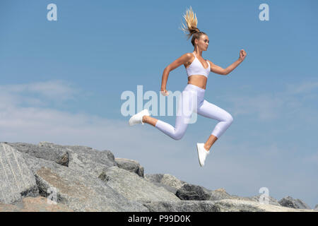 Attraktive sportliche Frau laufen und springen über Felsen, fit zu bleiben. Stockfoto