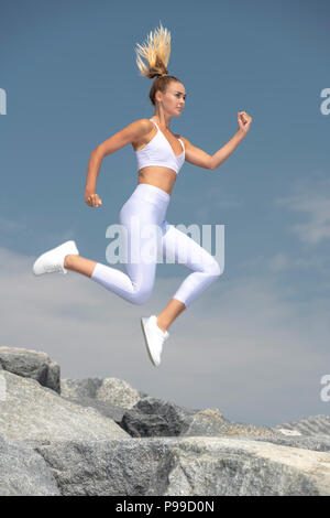 Attraktive sportliche Frau laufen und springen über Felsen, fit zu bleiben. Stockfoto