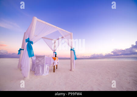 Romantisches Abendessen Tisch Set-up für eine Hochzeitsreise Paar am Strand unter Sonnenuntergang Himmel. Exotische Hochzeit und Flitterwochen Konzept Stockfoto