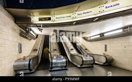 Mann und Frau Pendler mit Rolltreppe in die U-Bahn-Station Southwark in London Stockfoto