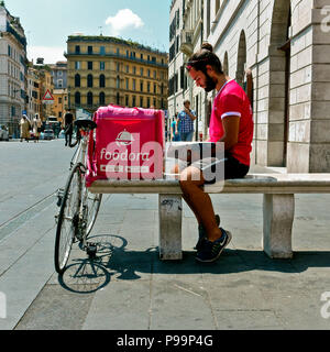 Austräger rufen Sie trägt ein rosa t-Shirt, ruht auf einer Bank und studieren während des Wartens auf eine Lieferung verlangen. Rosa Lieferbox Kurier. Rom, Italien Stockfoto