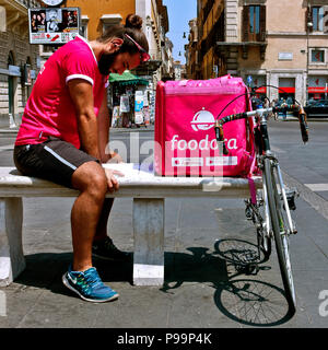 Austräger rufen Sie trägt ein rosa t-Shirt, ruht auf einer Bank und studieren während des Wartens auf eine Lieferung verlangen. Rosa Lieferbox Kurier. Rom, Italien Stockfoto