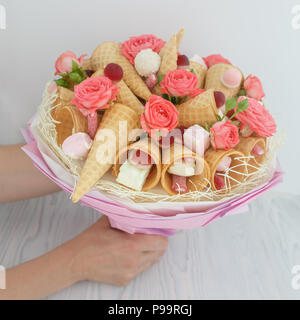 Blumenstrauß aus Blüten von Rosen, Waffeln, Süßigkeiten und Marshmallows in die weibliche Hände Stockfoto