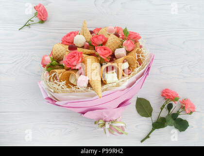 Blumenstrauß aus Blüten von Rosen, Waffeln, Süßigkeiten und Marshmallows auf einem hellen Hintergrund als originelles Geschenk Stockfoto