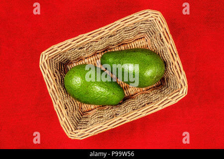 Table Top Blick auf zwei ganze avocado Obst im Korb, mit roten Tischdecke darunter. Stockfoto