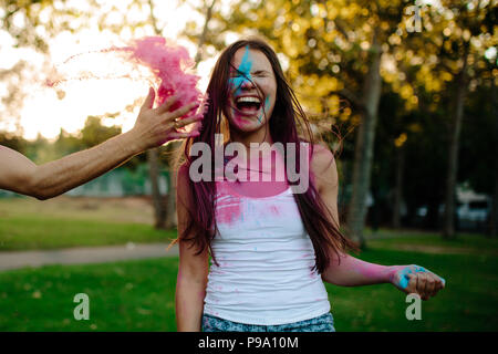 Frau im Park lachen während männlichen Freund werfen Farbe Pulver auf ihrem Gesicht. Freunde spielen mit Holi Festival im Park. Stockfoto