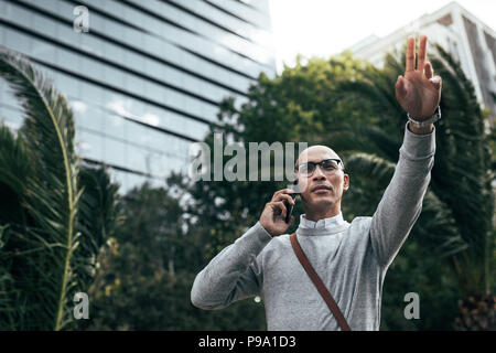 Geschäftsmann, der über Handy spricht, während er auf der Straße zur Arbeit läuft. Mann in Brille mit Bürotasche, der auf dem Handy telefoniert Stockfoto