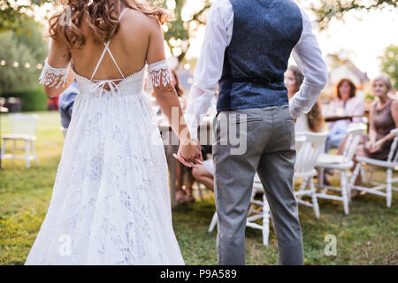 Nicht wiederzuerkennen, Braut und Bräutigam mit Gästen in Hochzeit außerhalb im Hinterhof. Stockfoto