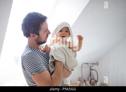 Vater mit einem Kleinkind Kind im Handtuch im Bad zu Hause eingepackt. Stockfoto