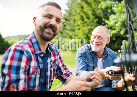 Ein erwachsener hipster Sohn und Vater Reparatur Fahrrad außerhalb an einem sonnigen Tag. Stockfoto