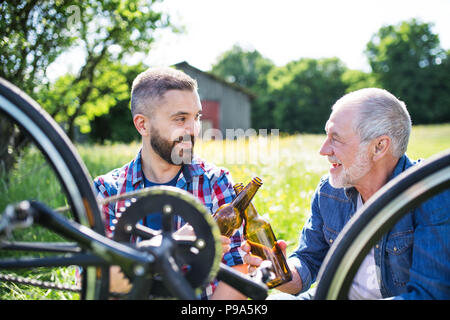 Ein erwachsener hipster Sohn und Vater Reparatur Fahrrad außerhalb an einem sonnigen Tag. Stockfoto