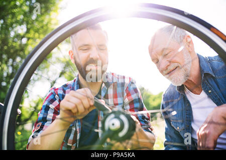 Ein erwachsener hipster Sohn und Vater Reparatur Fahrrad außerhalb an einem sonnigen Tag. Stockfoto