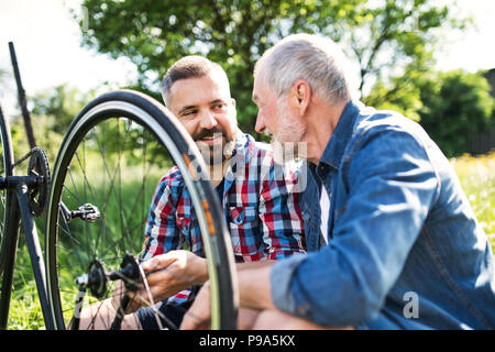 Ein erwachsener hipster Sohn und Vater Reparatur Fahrrad außerhalb an einem sonnigen Tag. Stockfoto