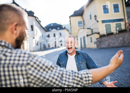 Ein erwachsener hipster Sohn und seine überglücklich senior Vater in der Stadt, Gruß. Stockfoto