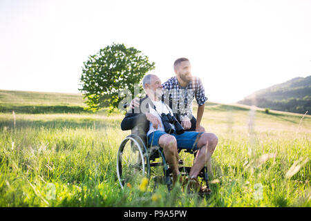 Ein erwachsener hipster Sohn mit dem Vater im Rollstuhl auf einen Spaziergang in der Natur bei Sonnenuntergang. Stockfoto