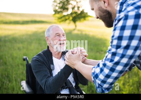 Ein erwachsener hipster Sohn mit dem Vater im Rollstuhl auf einen Spaziergang in der Natur bei Sonnenuntergang. Stockfoto