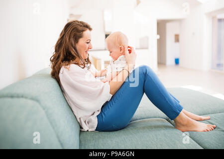 Junge Mutter mit Baby Boy zu Hause auf dem Sofa sitzen. Stockfoto