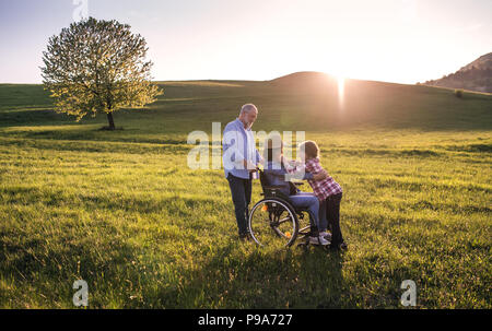 Ein kleines Mädchen mit ihrem älteren Großeltern mit Rollstuhl auf einem Spaziergang in der freien Natur. Stockfoto