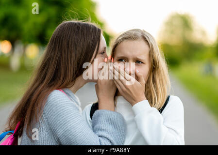 Zwei Freundinnen Schülerinnen, Schüler. Im Sommer Stadt. Sagt ein Freund Ohr, ein Geheimnis, wirklich. Das Konzept der Überraschung, beste Freunde, Angst, Groll. Emotionen sind Angst, enttäuscht, unwahr, Stockfoto