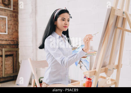 Seitenansicht Porträt der hübsche junge Frau Malerei Staffelei saß in art studio Stockfoto