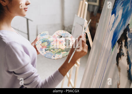 Mitte Porträt der jungen Künstlerin Holding palette Malen an der Staffelei im Atelier stehend gegen Windows im Sonnenlicht, kopieren Raum Stockfoto