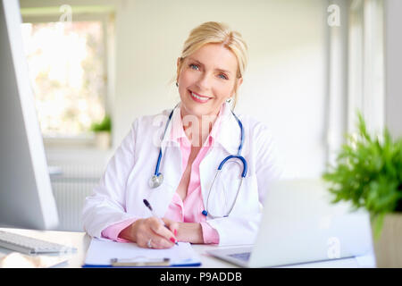 Nahaufnahme Porträt der leitenden Ärztin im Arzt Büro am Schreibtisch vor Laptop und dabei einige Schreibarbeit. Stockfoto