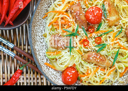 Rühren gebratene Nudeln mit Huhn, Gemüse (Karotten, Tomaten, Zucchini, Knoblauch, Paprika, grüne Zwiebeln), Sesam und Soja Sauce auf Lehm Platte schließen Stockfoto