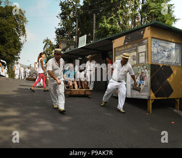 Touristen genießen die Fahrt bergab auf einem traditionellen Weidenkorb Rodeln auf den Straßen über Funchal, Madeira Stockfoto