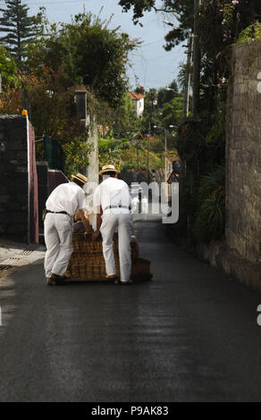 Touristen genießen die Fahrt bergab auf einem traditionellen Weidenkorb Rodeln auf den Straßen über Funchal, Madeira Stockfoto
