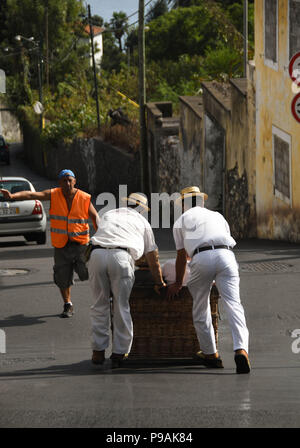 Touristen genießen die Fahrt bergab auf einem traditionellen Weidenkorb Rodeln auf den Straßen über Funchal, Madeira Stockfoto