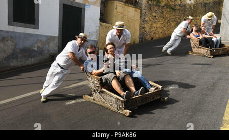 Touristen genießen die Fahrt bergab auf einem traditionellen Weidenkorb Rodeln auf den Straßen über Funchal, Madeira Stockfoto