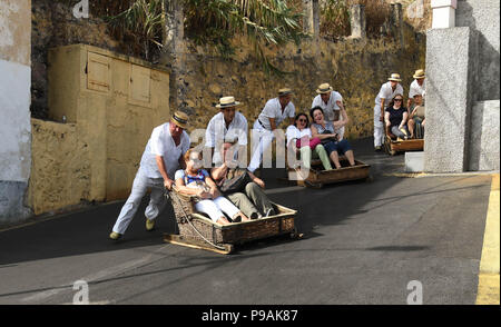 Touristen genießen die Fahrt bergab auf einem traditionellen Weidenkorb Rodeln auf den Straßen über Funchal, Madeira Stockfoto