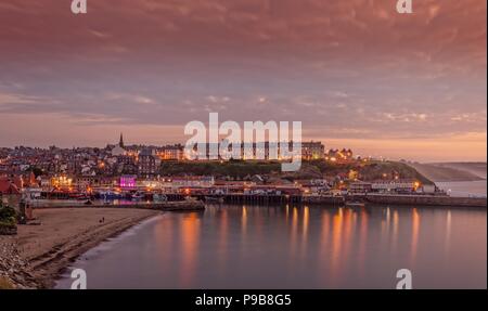 Eine Ansicht von Whitby Stadt nachts aus der ganzen äußeren Hafen. Die Häuser und Geschäfte sind beleuchtet und eine dicke Wolke ist Overhead. Stockfoto