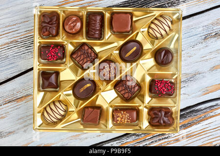 Verschiedene Pralinen in goldenem Feld. Gruppe von köstlichen Pralinen auf hölzernen Hintergrund, Ansicht von oben. Süßes Geschenk für Valentines Tag. Stockfoto