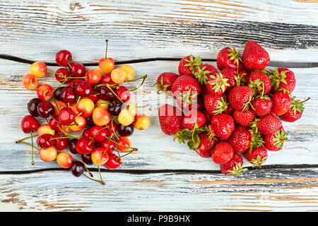 Haufen Erdbeeren und Kirschen, Ansicht von oben. Reife Beeren auf vintage Holz- Hintergrund. Frisch aus dem Garten. Stockfoto