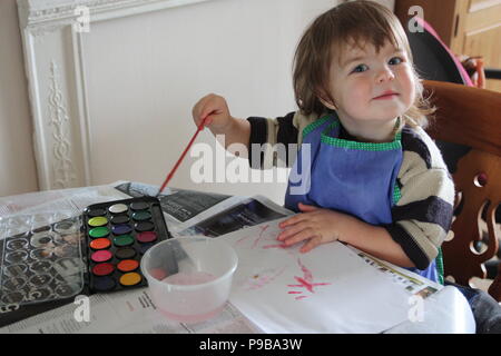 Nette junge Mädchen in gestreiften Pullover Malerei in Schürze mit Aquarellfarben an einem Tisch sitzen Stockfoto