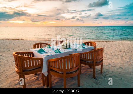 Erstaunliche Familie Tisch Set-up an einem tropischen Strand im Sonnenuntergang. Beruhigende Szene für Abendessen am Strand Stockfoto