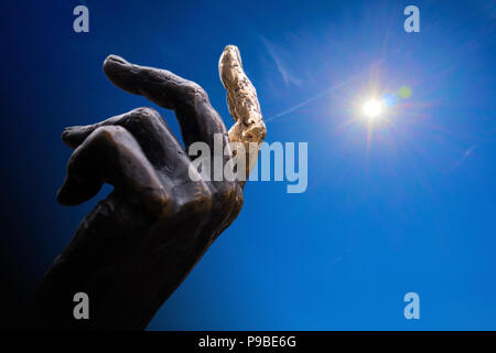 Hand aus Bronze Statue mit einem Finger zeigt zum Himmel, Konzept collage gegen den blauen Himmel und Sonne mit Heiligenschein Stockfoto