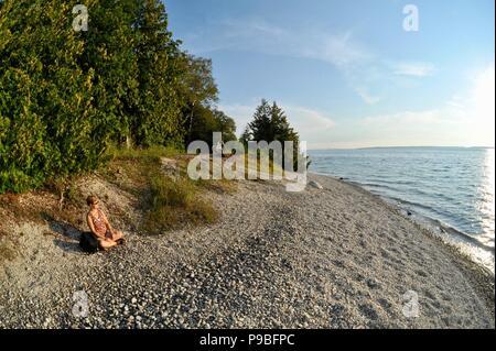 Frau sitzen und entspannen bei Sonnenuntergang am Strand beobachten, Sun Set über Lake Huron, auf Mackinac Island, Michigan, USA. Stockfoto