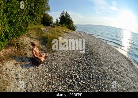 Frau sitzen und entspannen bei Sonnenuntergang am Strand beobachten, Sun Set über Lake Huron, auf Mackinac Island, Michigan, USA. Stockfoto